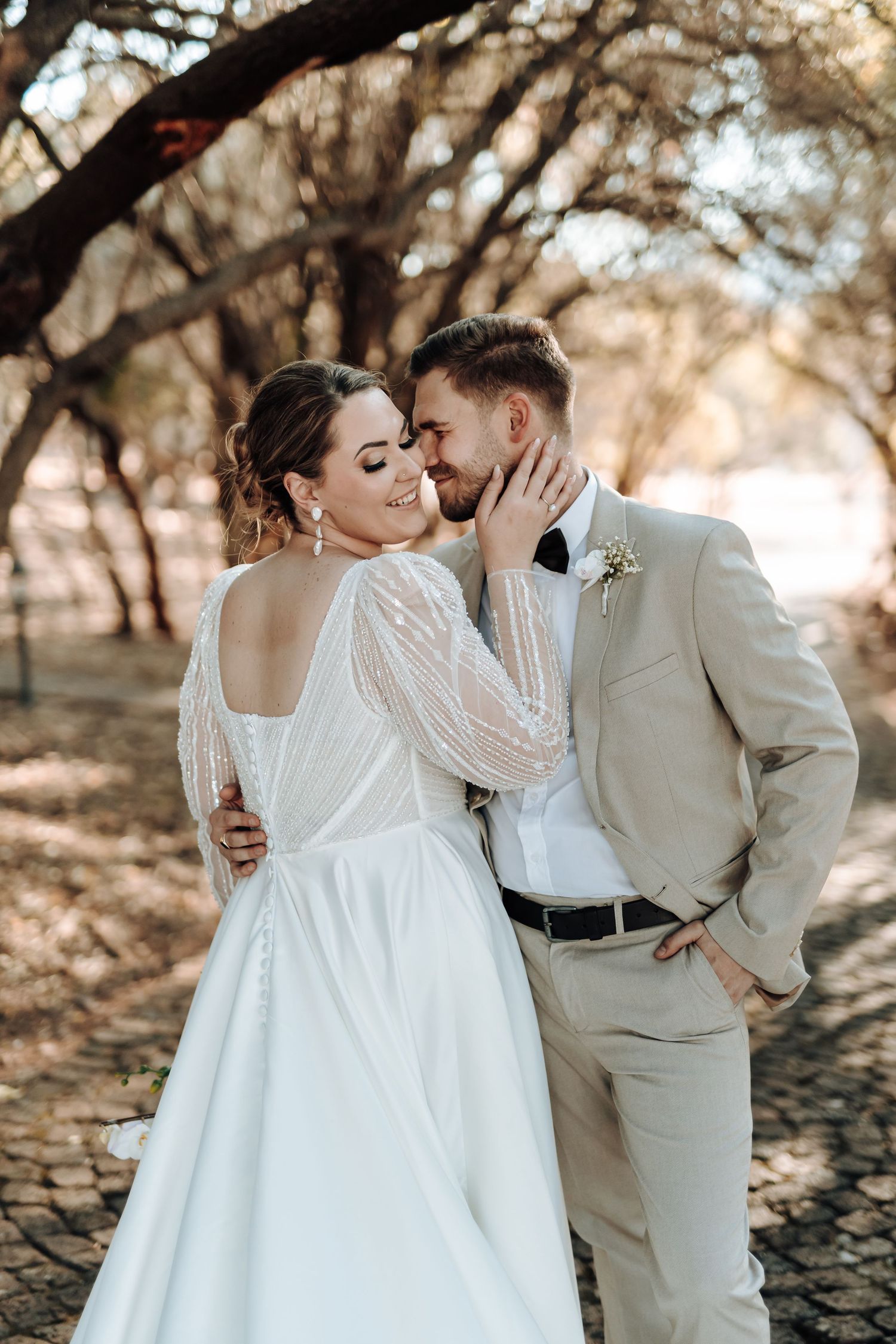 Intimate moment between newlyweds in beige and white attire beneath autumn trees.