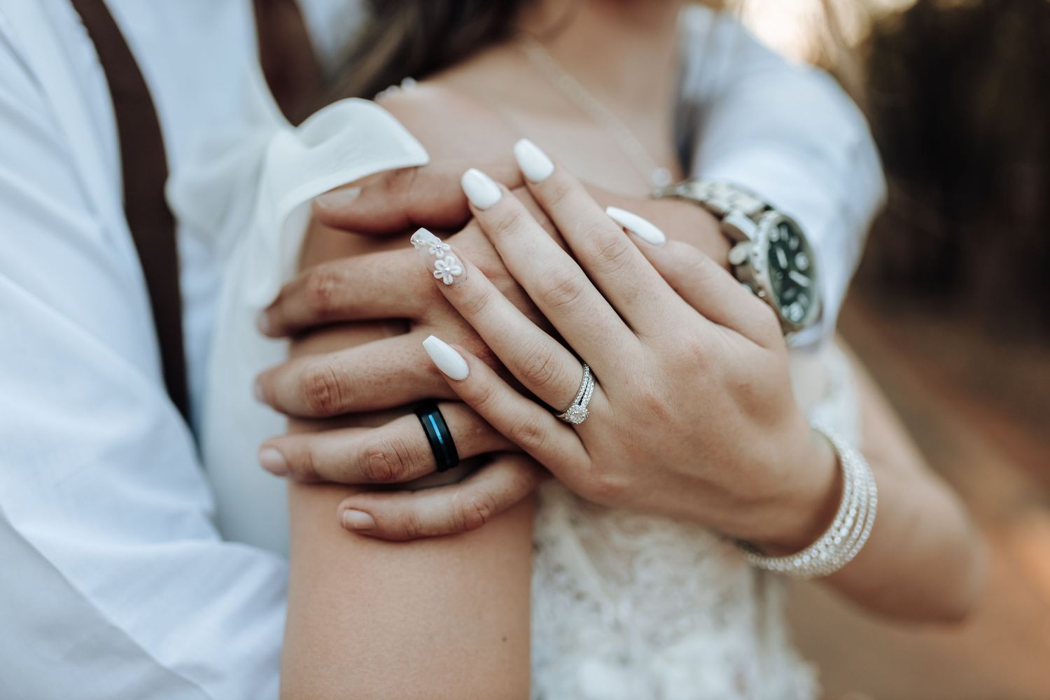 Close-up of hands wearing wedding rings against white lace and fabric.