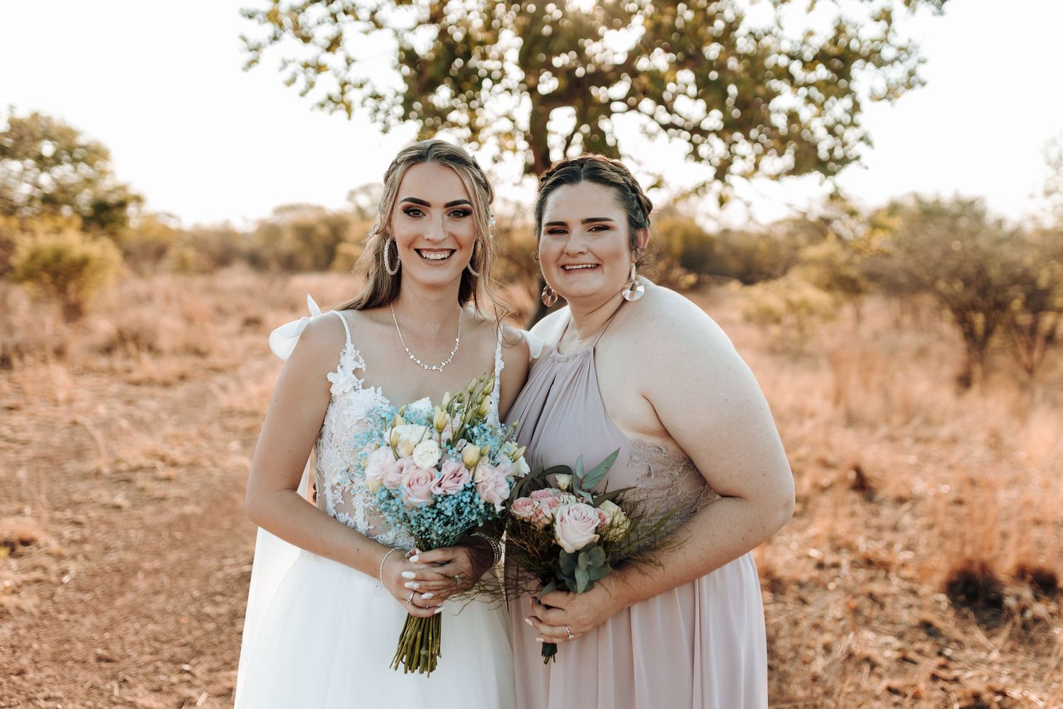 Two people wearing formal attire holding bouquets of blue and white flowers in an outdoor setting.