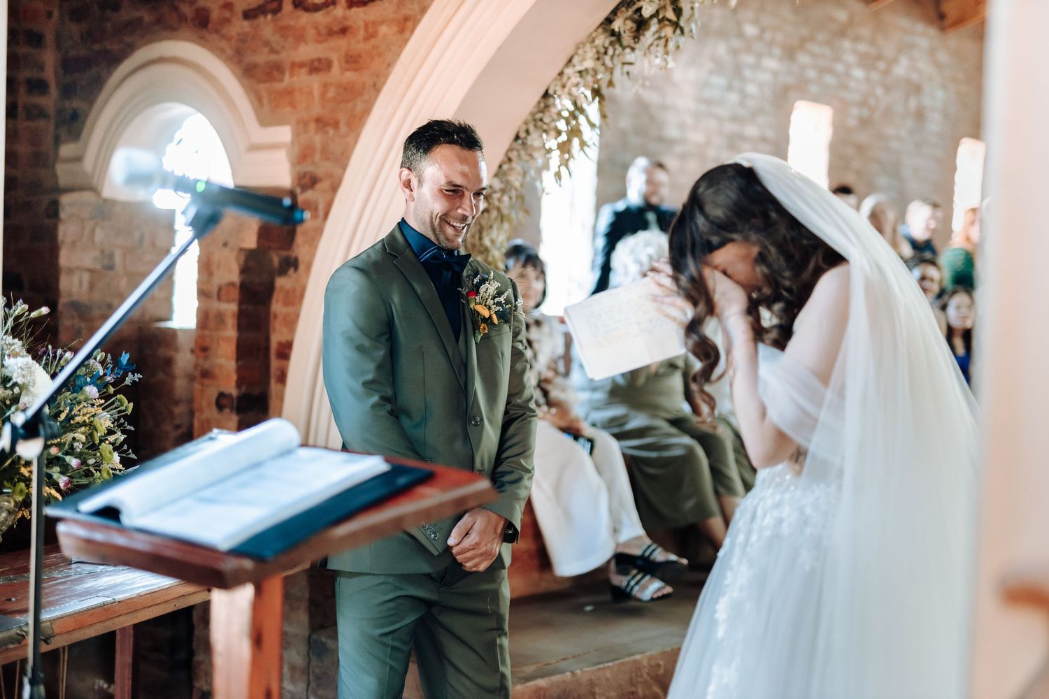 Couple shares emotional moment during wedding ceremony in brick chapel with floral decorations.