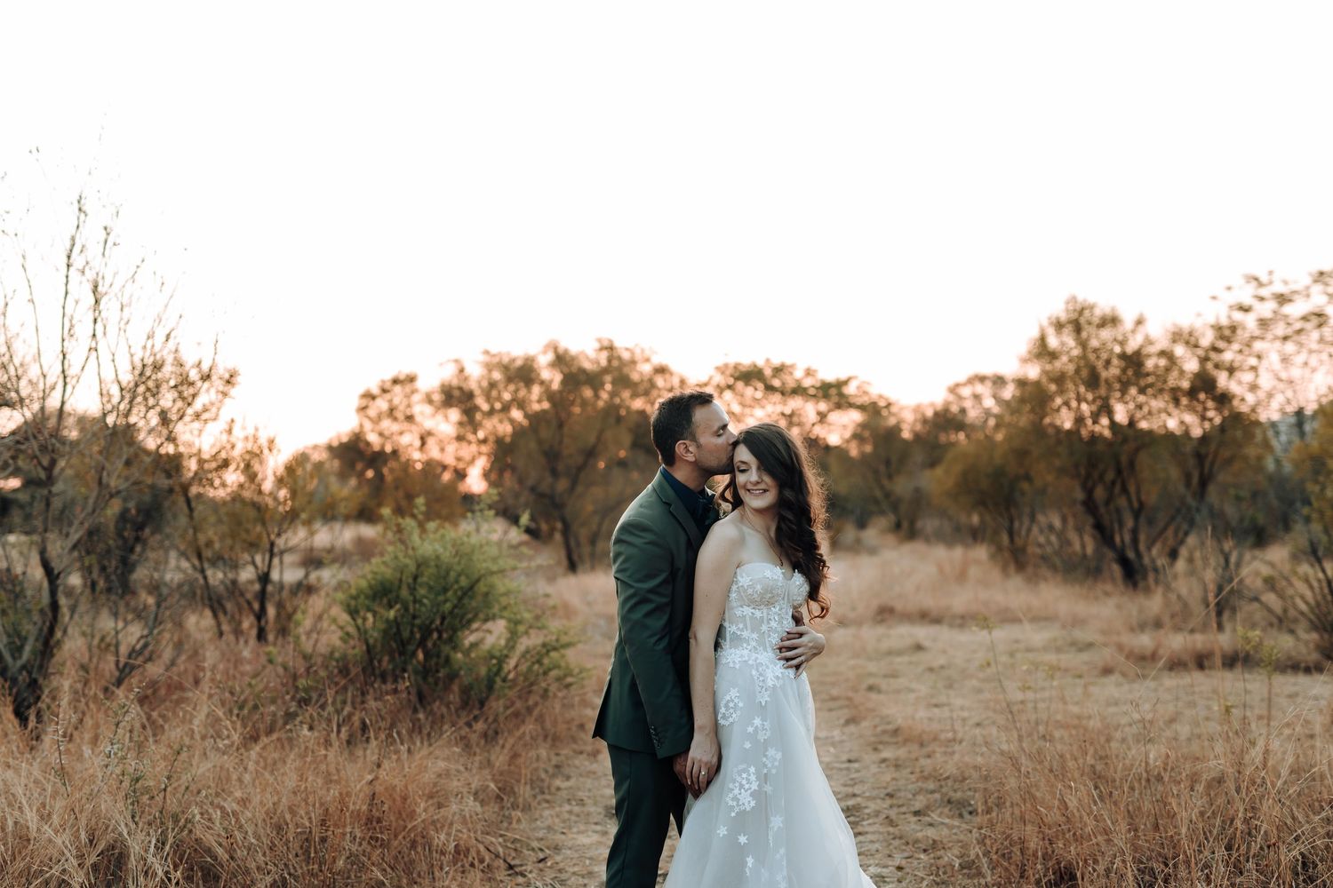 Romantic candid moment between newlyweds on a rural path at sunset.