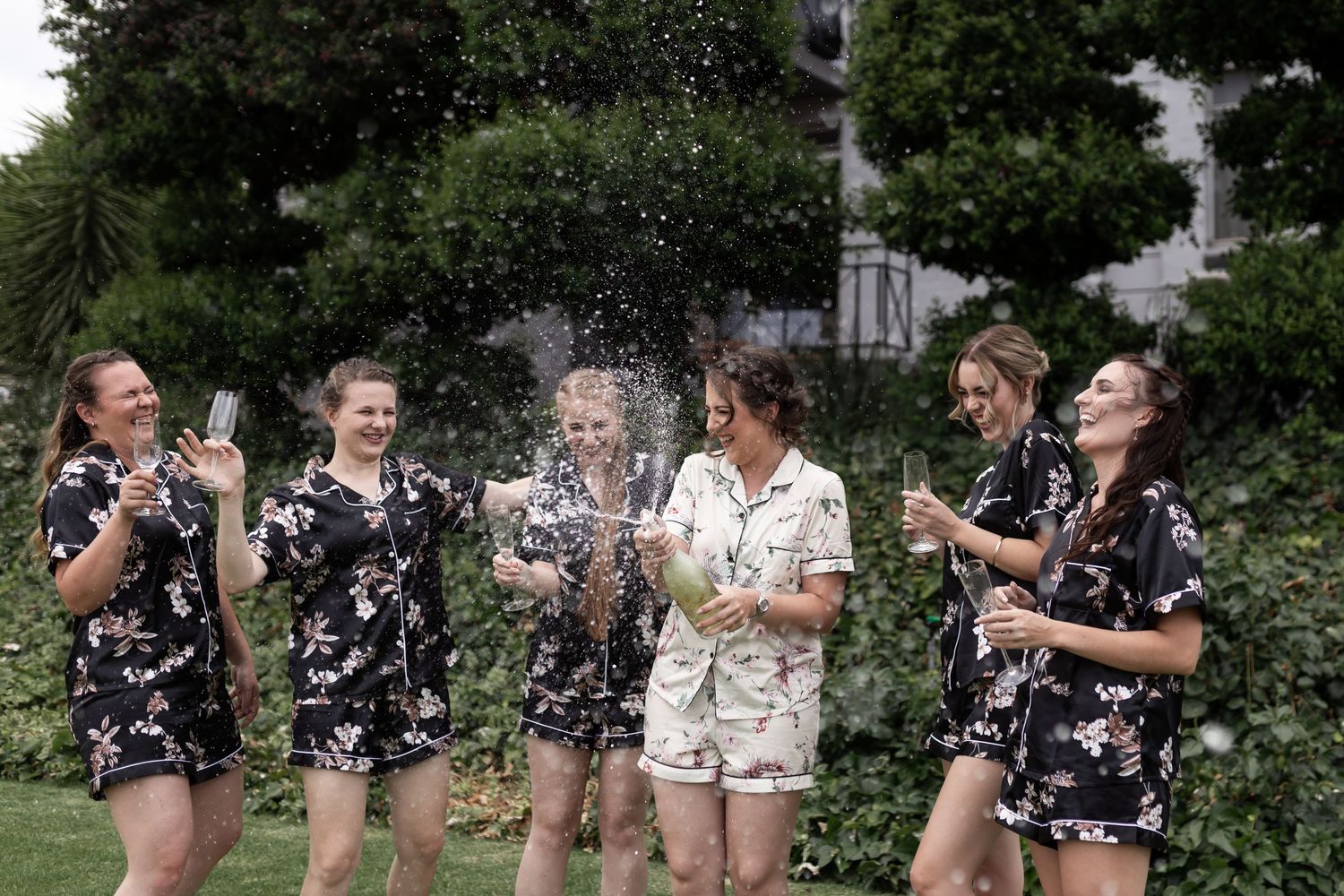 Celebratory moment captured with champagne spray in outdoor garden setting.