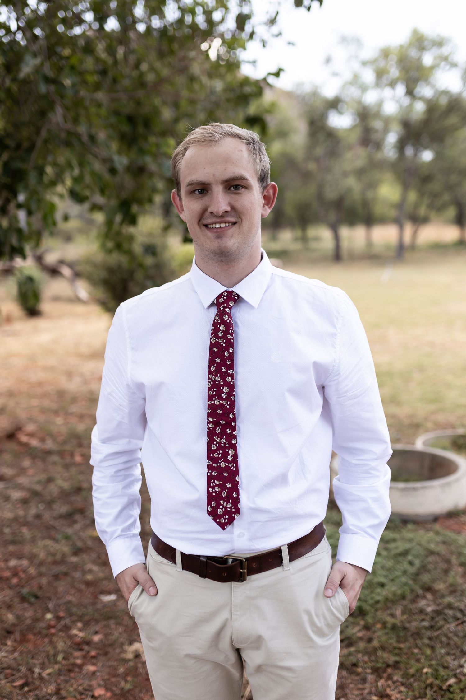Wedding party member in crisp white shirt and polka dot tie poses outdoors.