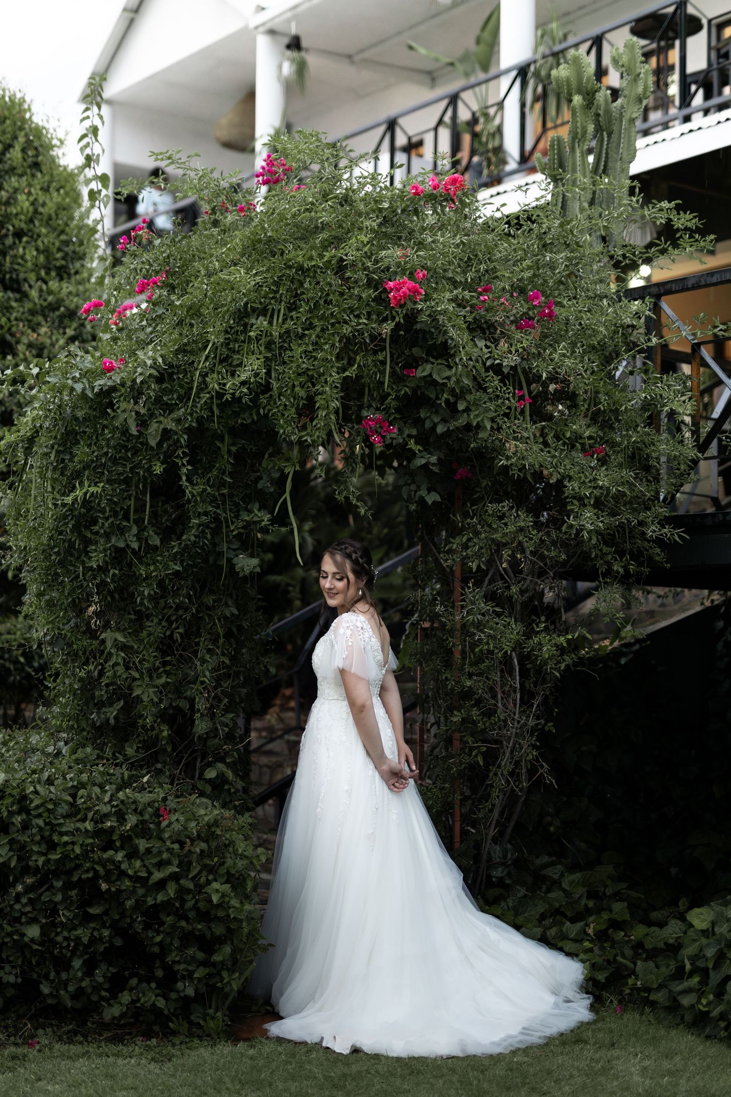 Elegant white wedding gown photographed against lush garden with climbing roses.