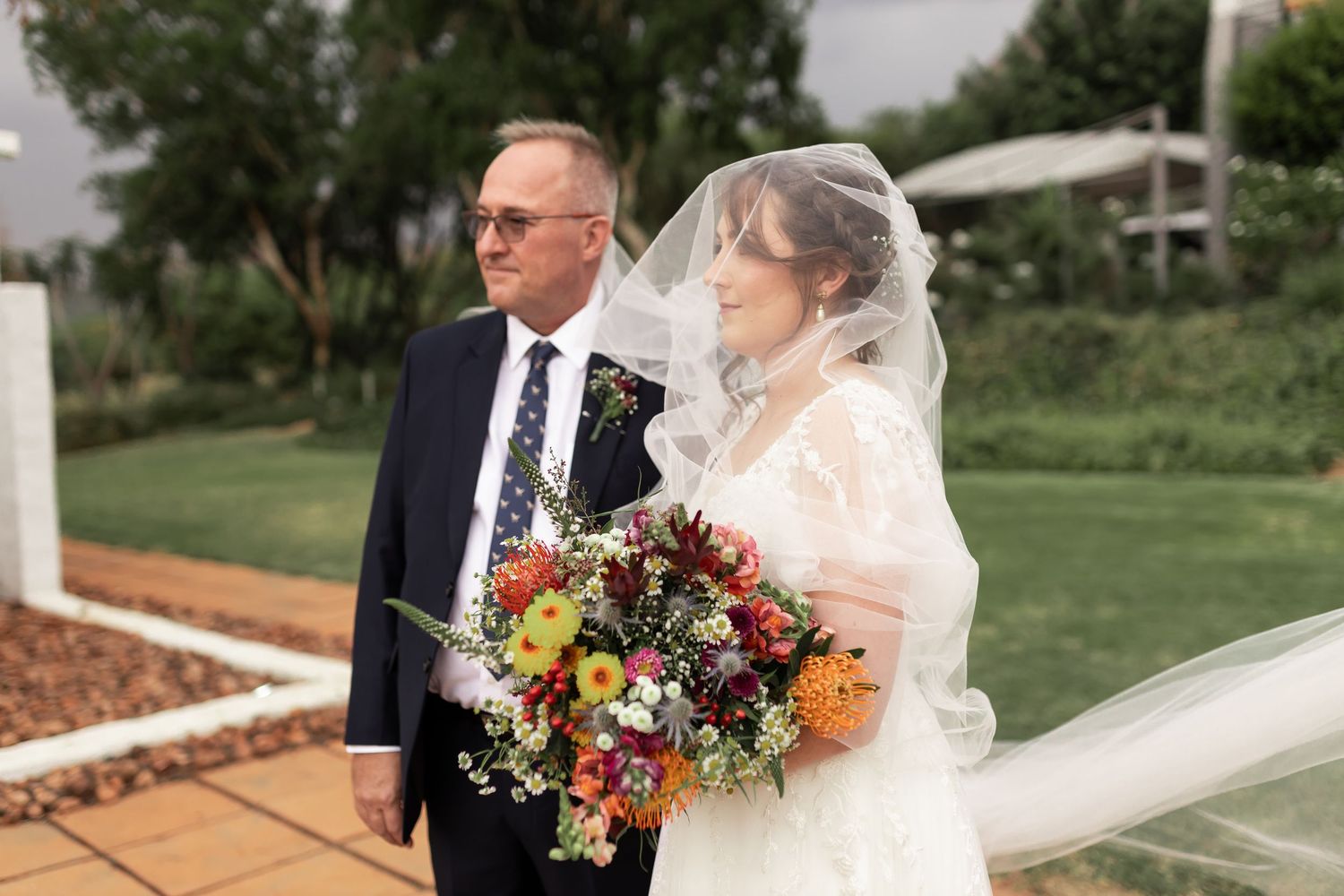 A touching outdoor wedding moment with a stunning colorful bouquet against a garden backdrop.
