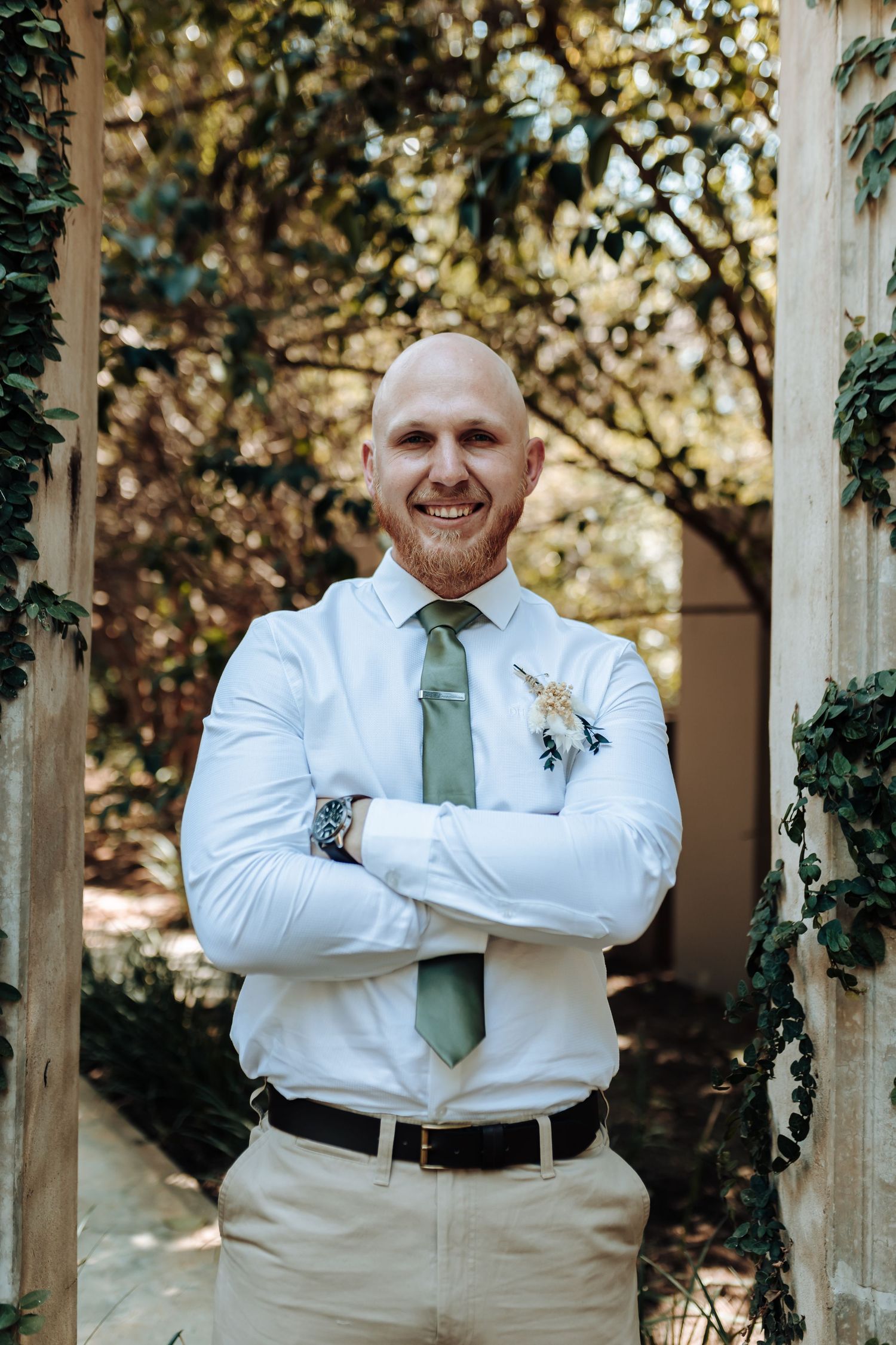 Person in white dress shirt and sage tie poses confidently against garden archway.