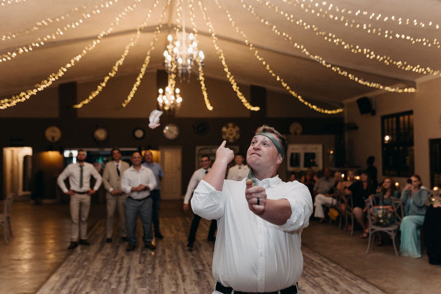 Wedding reception performer singing with microphone under romantic string lights in rustic venue.
