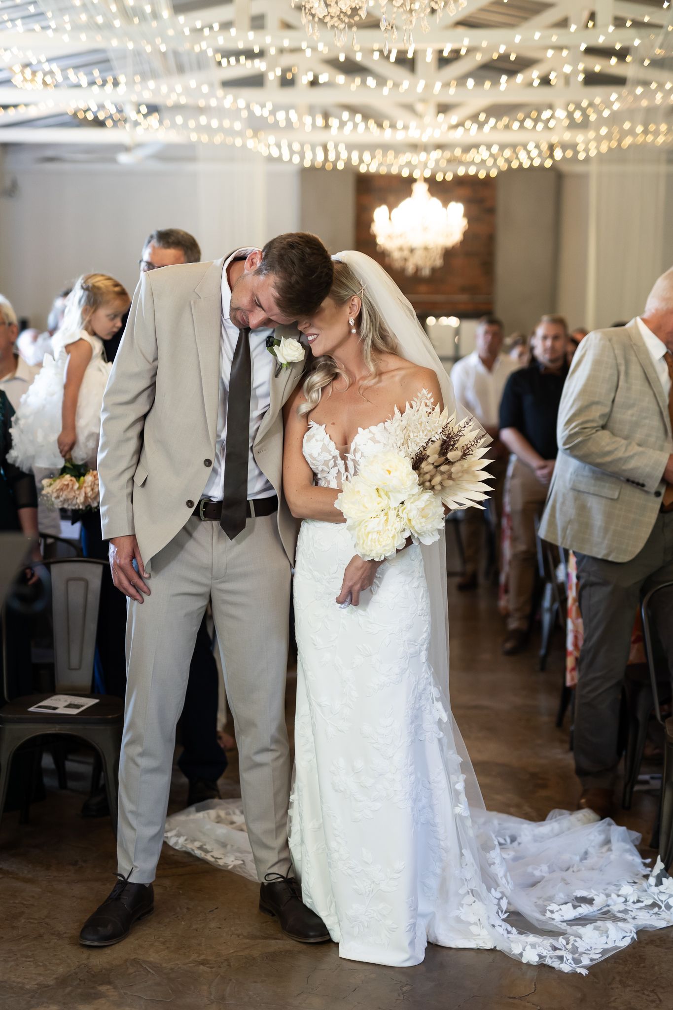 Intimate moment between couple during wedding reception with string lights overhead.