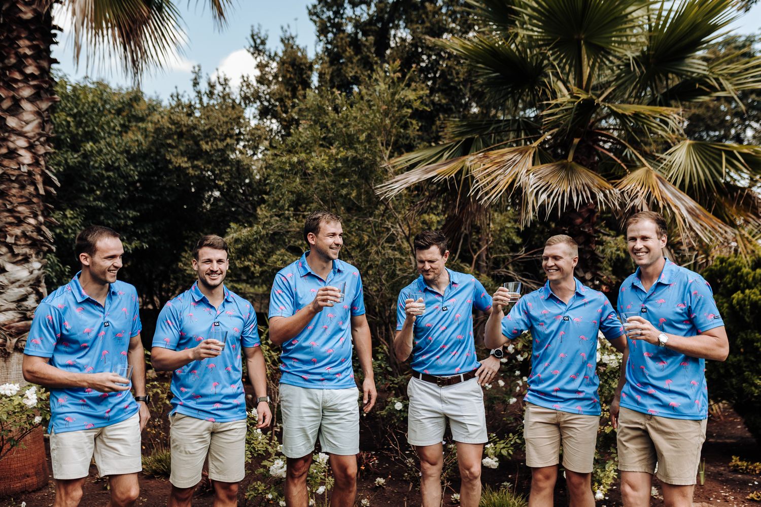Groomsmen in matching light blue polo shirts and khaki shorts posing outdoors.