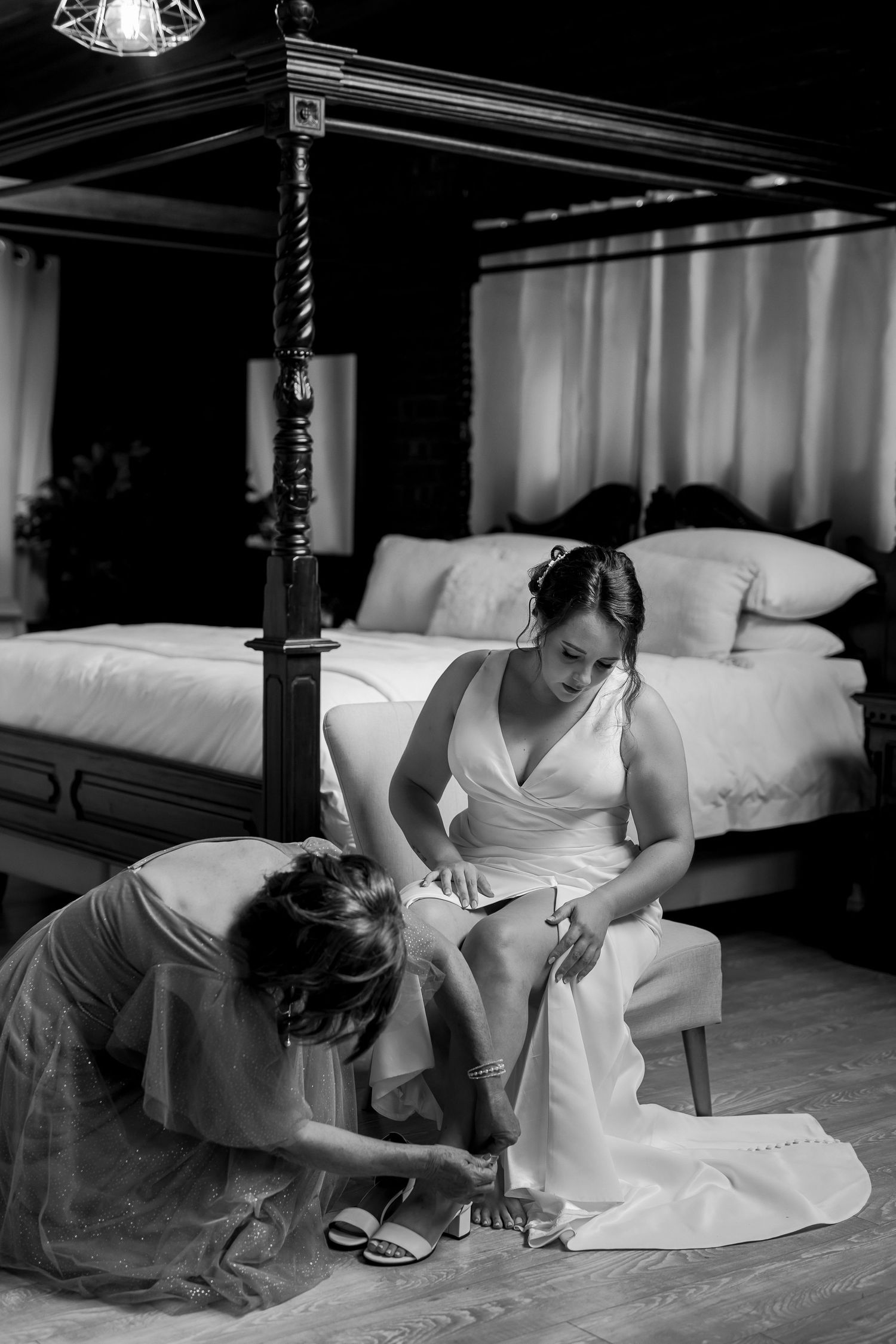 Black and white capture of wedding dress preparation in bedroom setting.