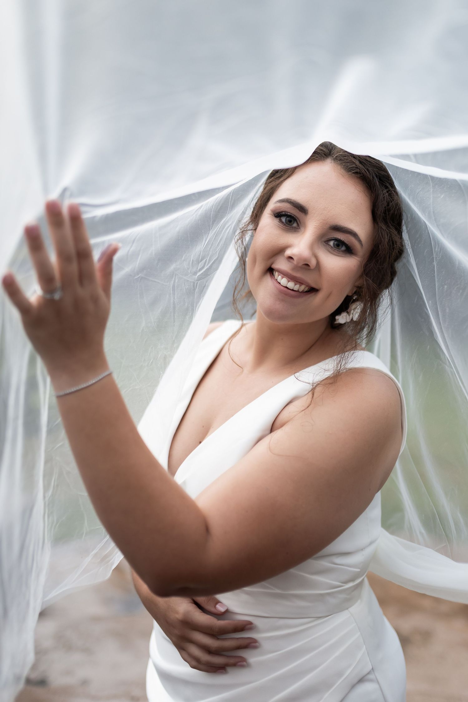 Playful moment under flowing white veil against soft background.