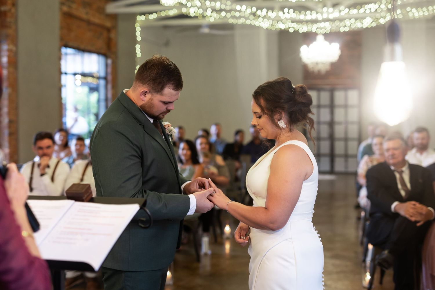 Wedding ceremony with ring exchange under elegant lighting and exposed brick walls.