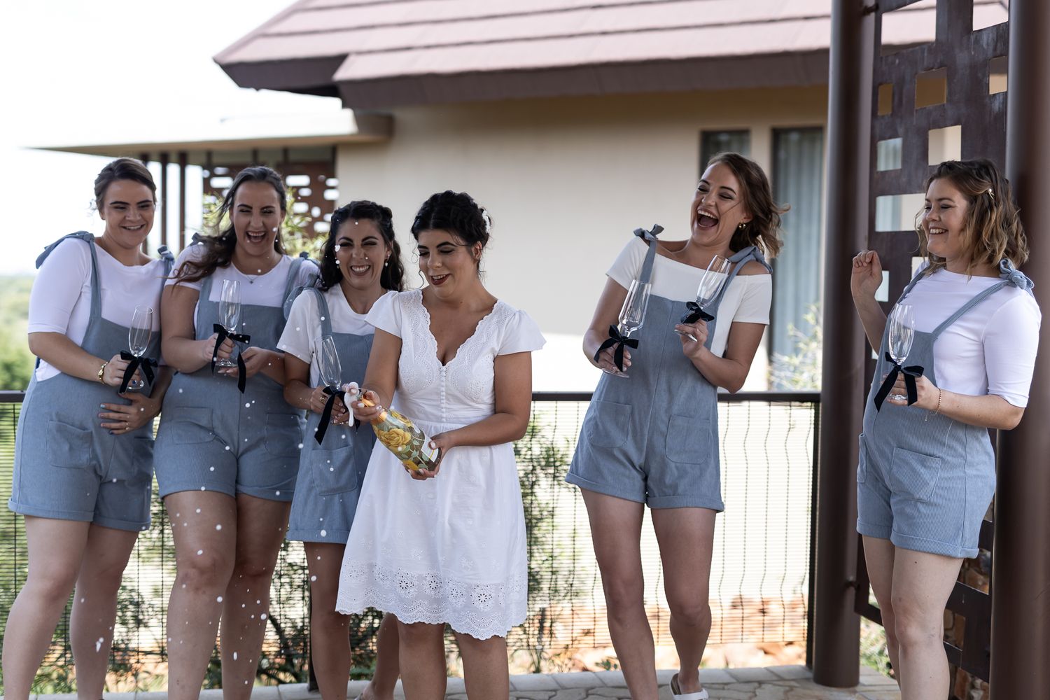 Group wearing coordinated blue overalls and white shirts holding drinks outdoors.