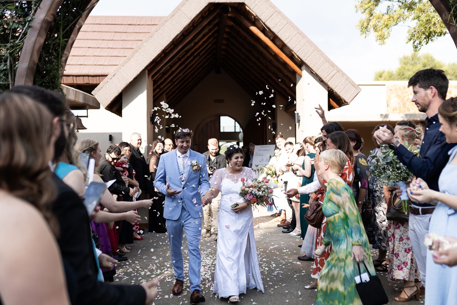 Newlyweds exit their wedding ceremony as guests shower them with flower petals.