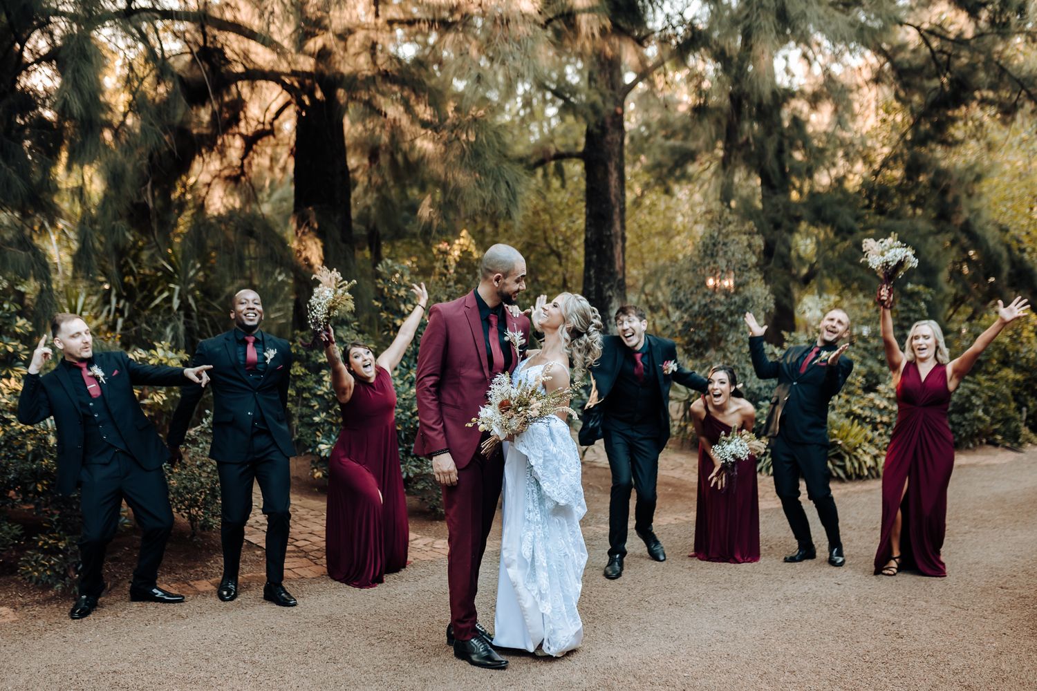 Wedding party celebrates joyfully on garden path with couple in center.