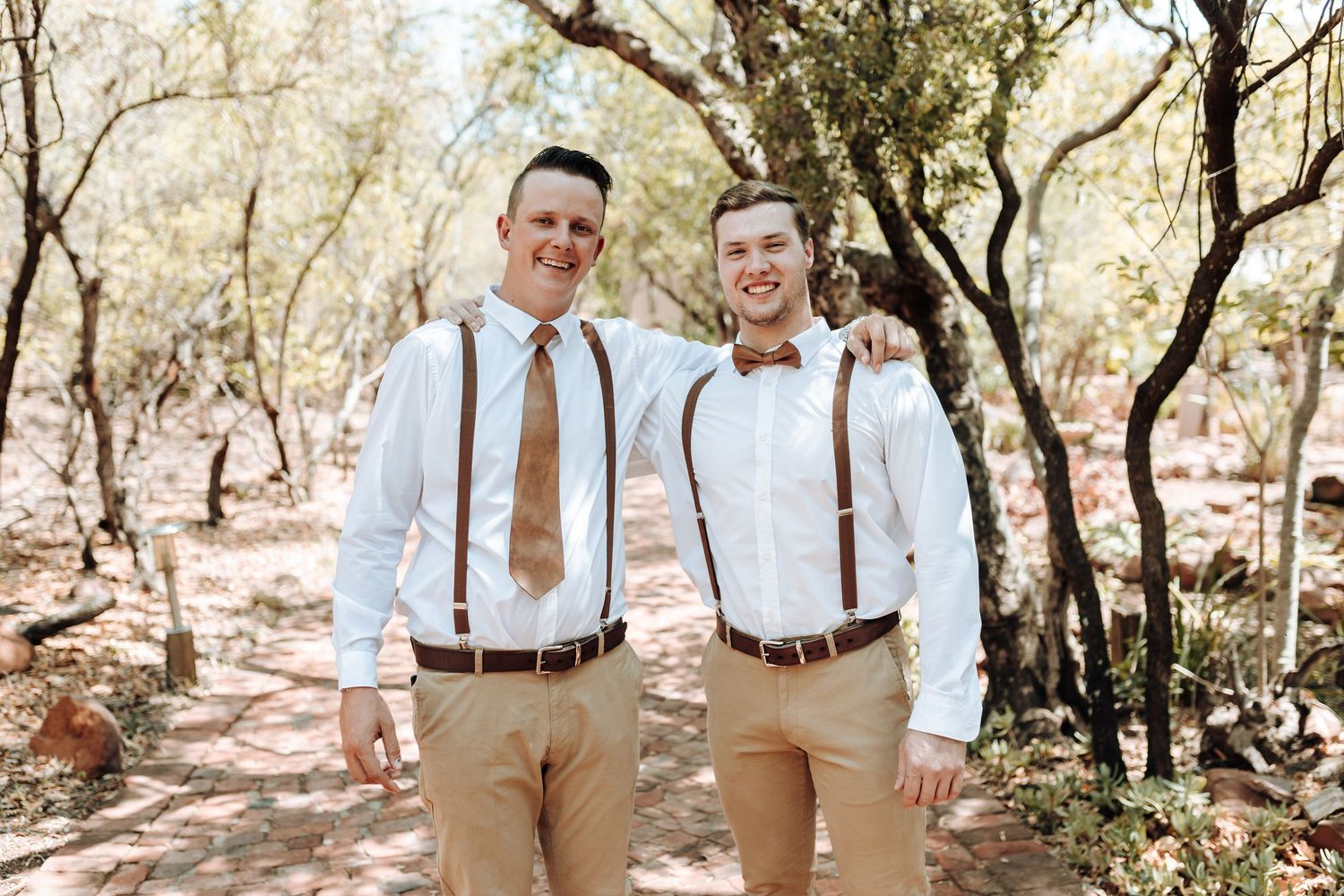 Two people in coordinated white shirts and tan pants share a moment outdoors.
