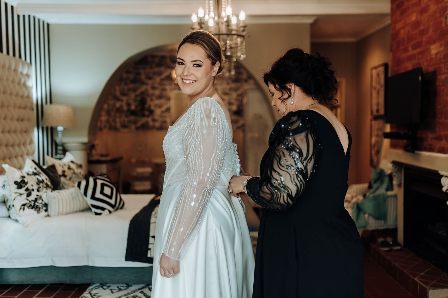 Bride in classic white gown with sparkly long sleeves getting ready in elegant room.
