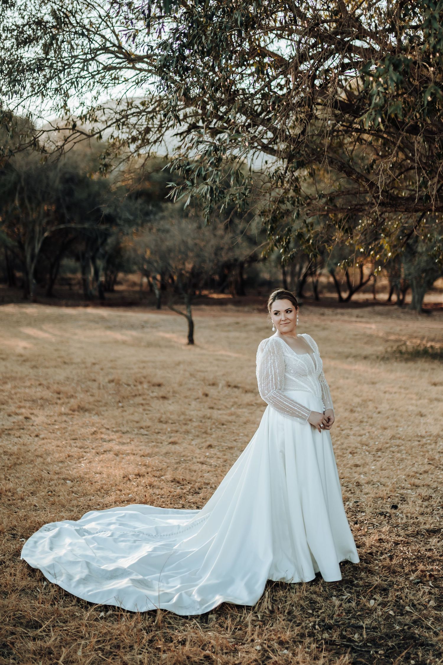 Dramatic bridal portrait showing flowing train of white wedding gown in outdoor setting.