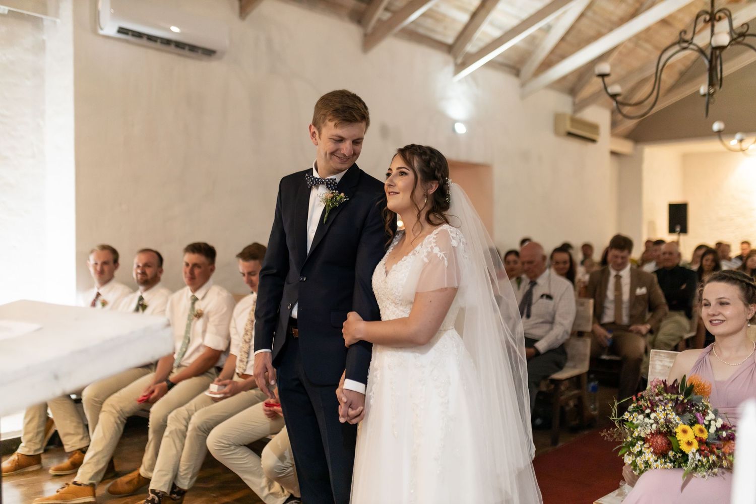 A couple participates in their wedding ceremony in a bright venue with exposed beams.