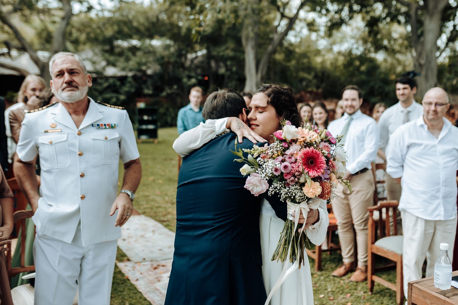 Emotional wedding ceremony moment in garden setting with military dress uniform visible.