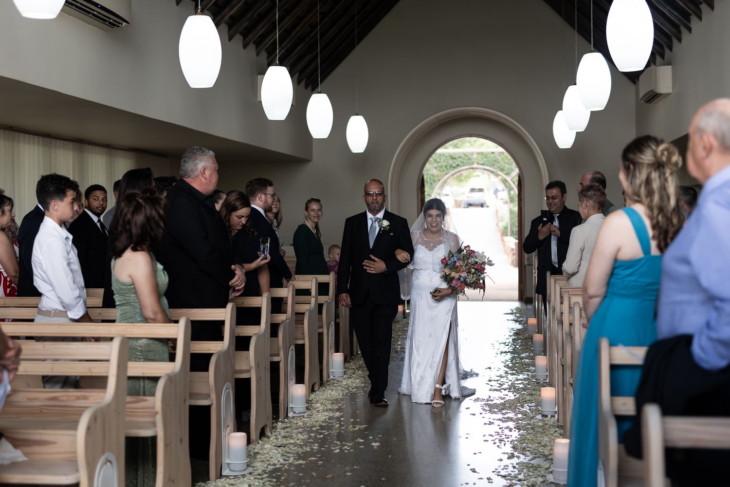 Wedding ceremony in modern church with pendant lights and wooden pews.