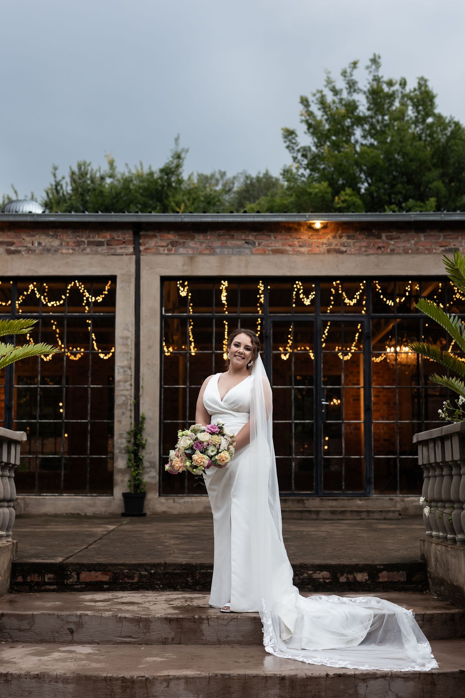 Elegant bridal portrait in front of industrial brick building with twinkling string lights.