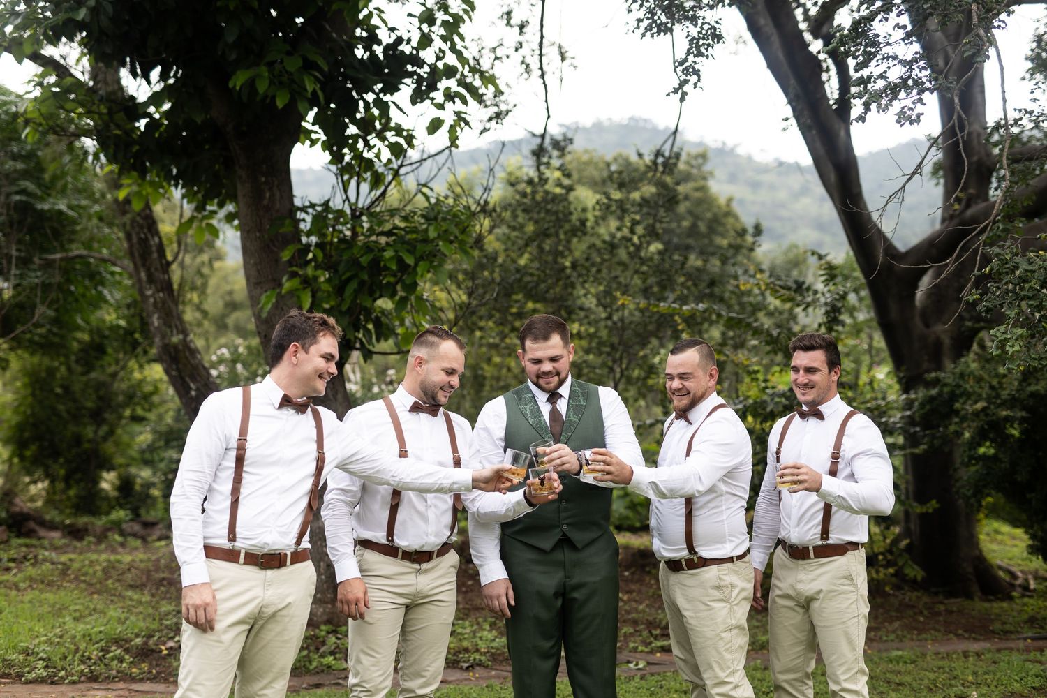 Groomsmen in matching attire gather around looking at something in an outdoor setting.