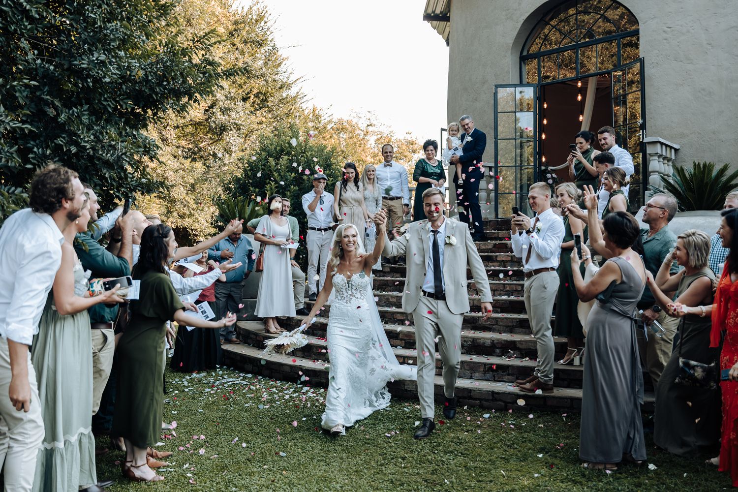 Wedding party and guests gather on church steps during an outdoor celebration.