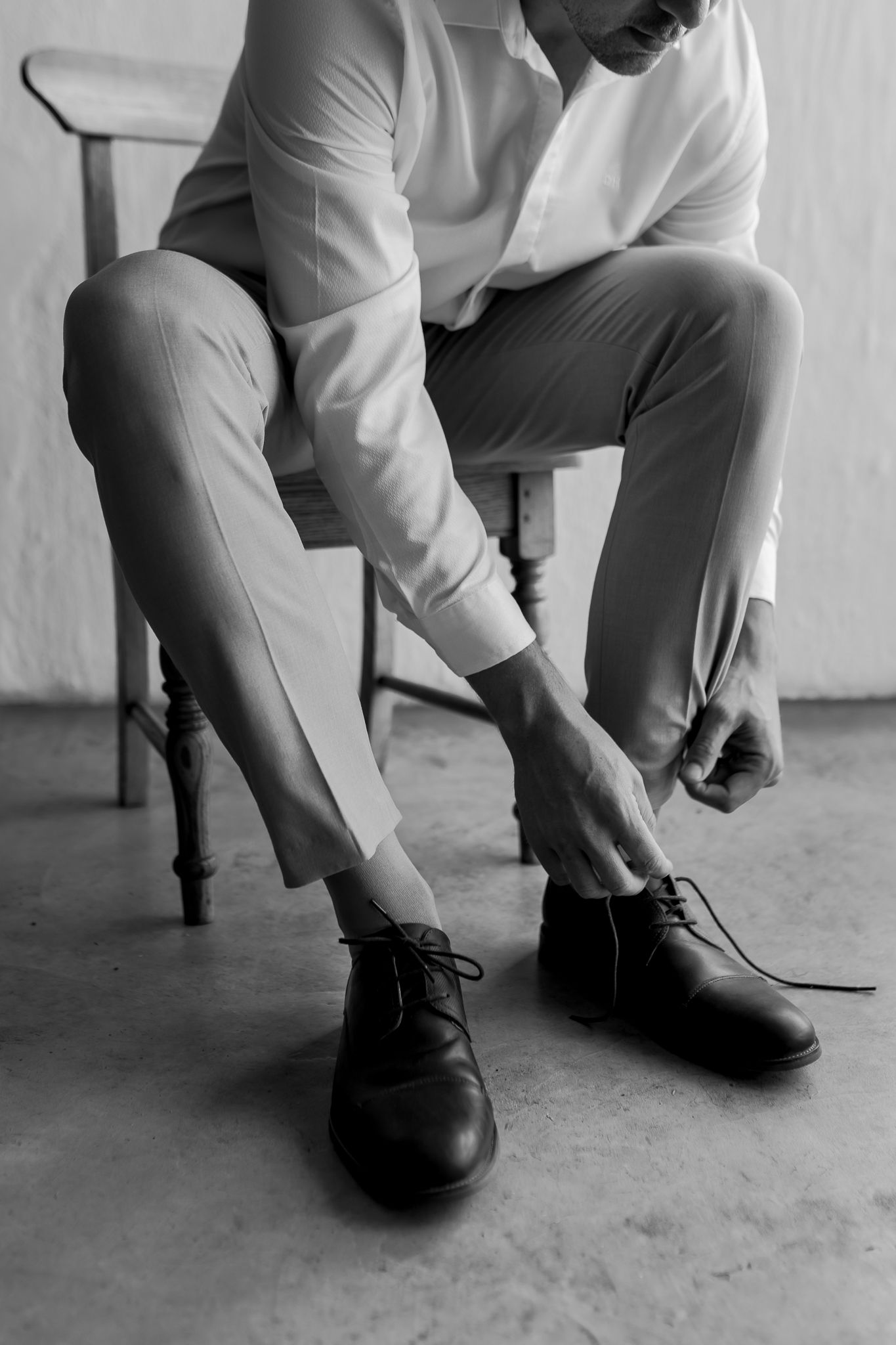 Close-up black and white shot of someone tying leather dress shoes while sitting in a chair.
