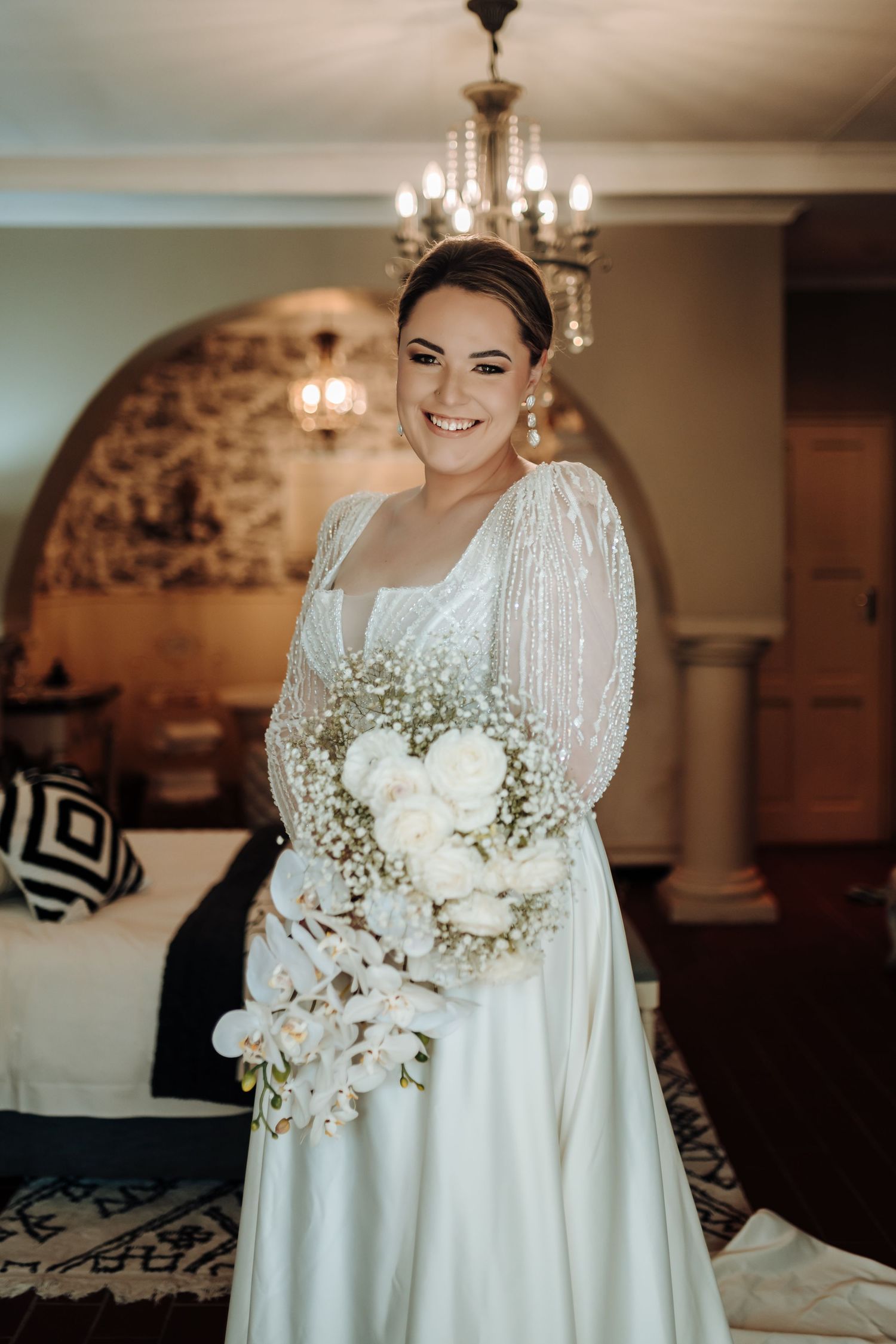 Radiant bride holding white floral bouquet in elegant room with chandelier.