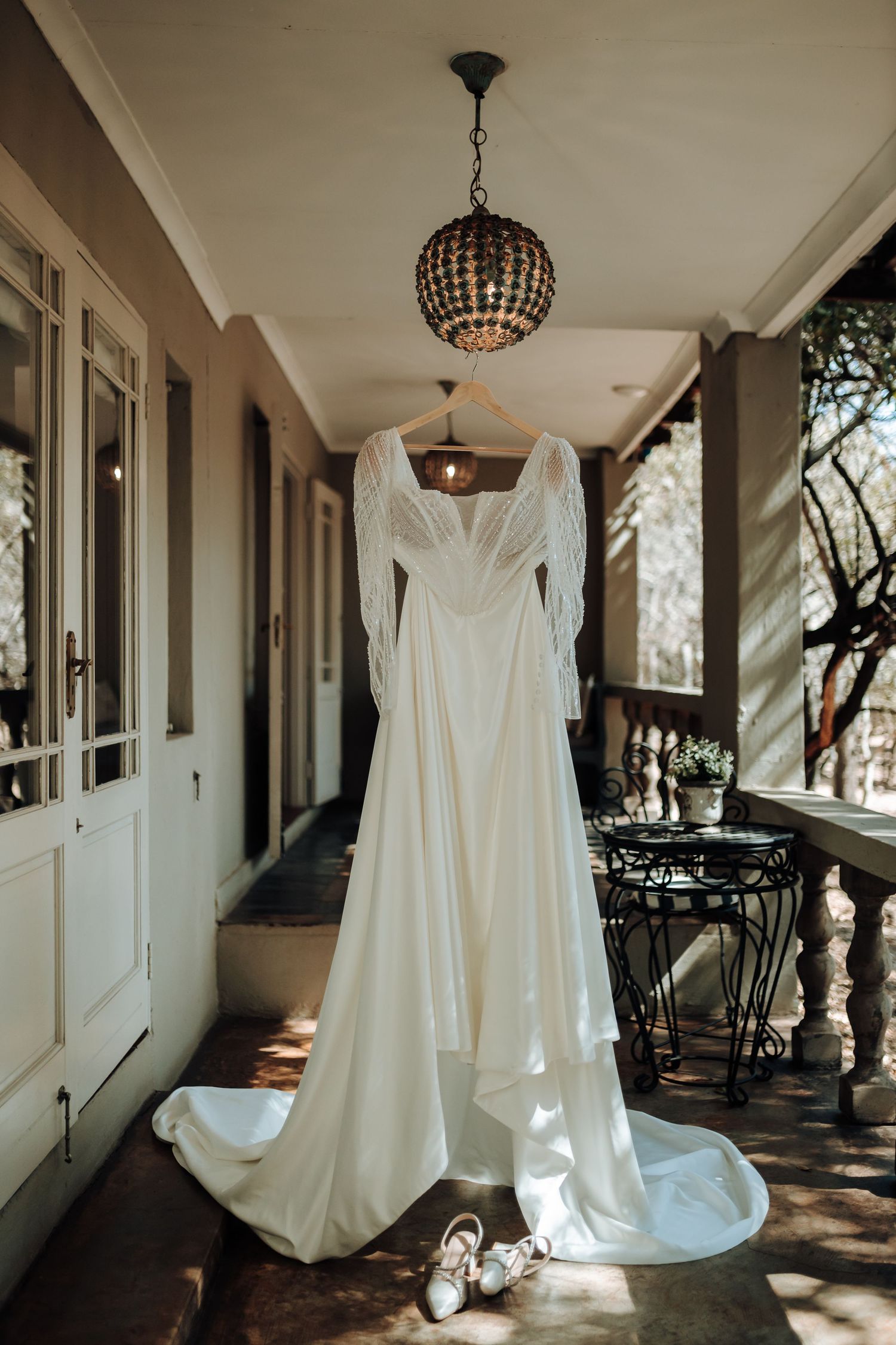An elegant white wedding dress hanging from a chandelier in a vintage hallway.