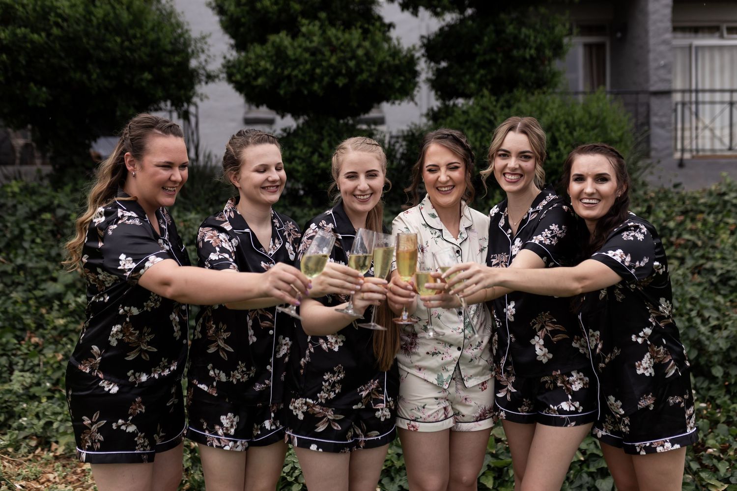 Group toasts with champagne glasses in outdoor garden setting.