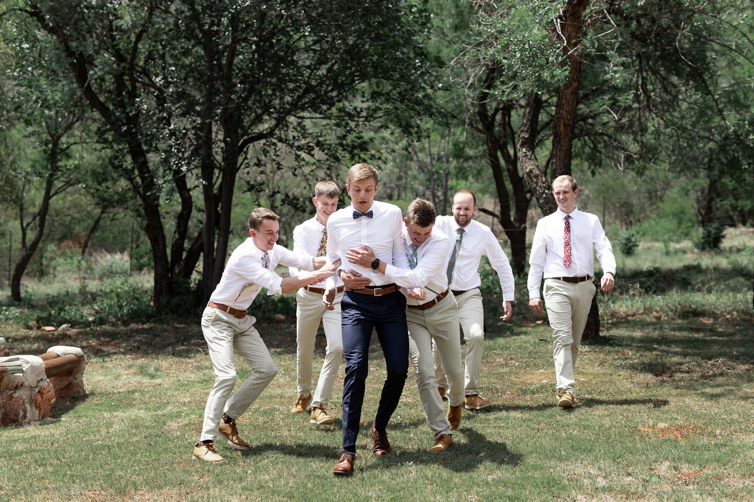 Wedding party playfully poses together outdoors in matching white shirts and khaki pants.