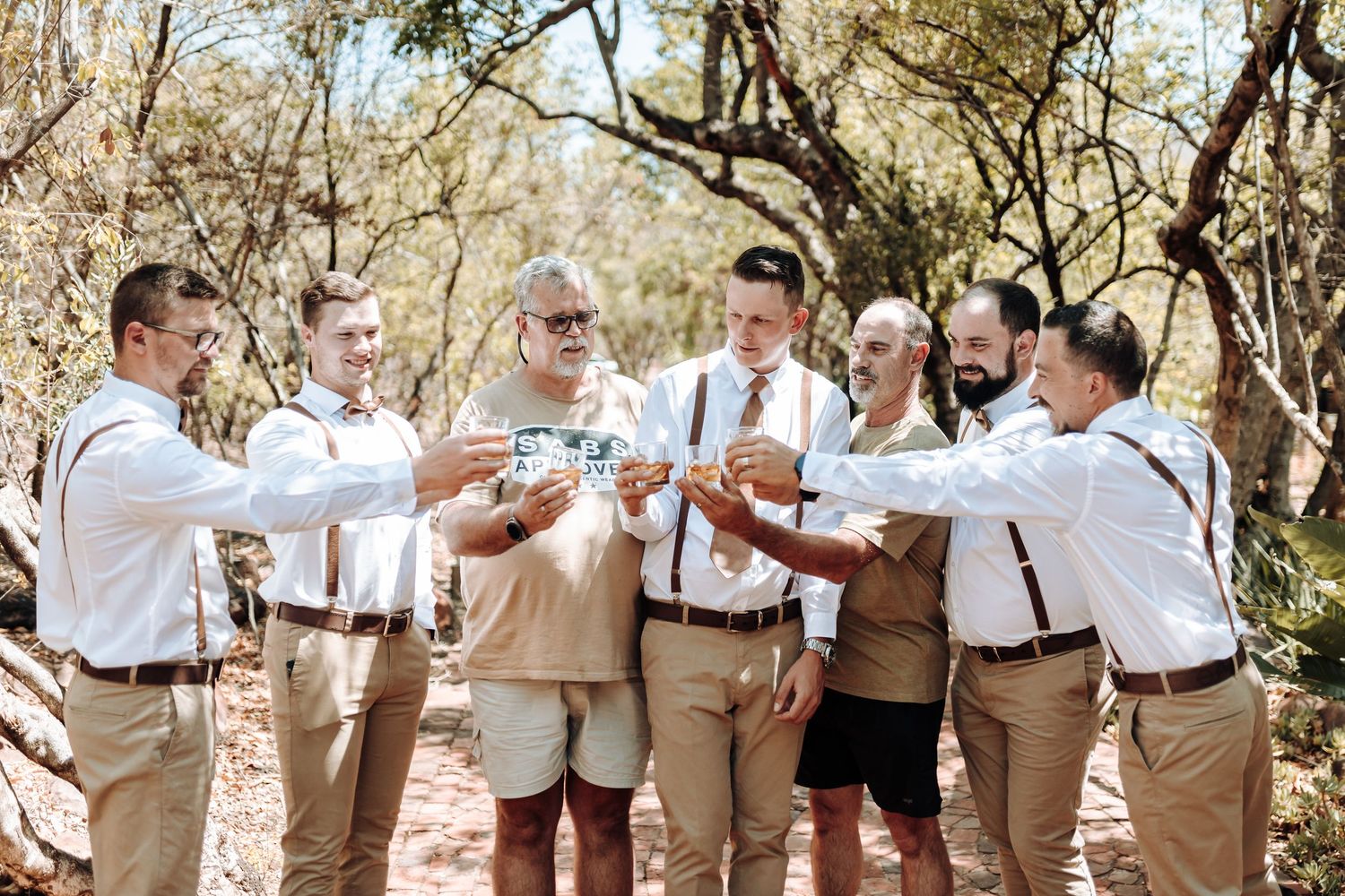 Group in matching casual formal wear toasting outdoors among trees.