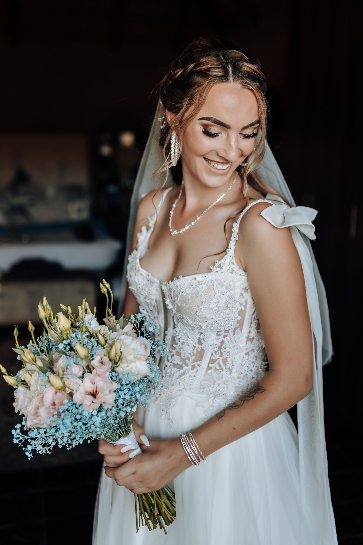 Elegant bride in lace dress holding a blue and pink wedding bouquet with a soft smile.