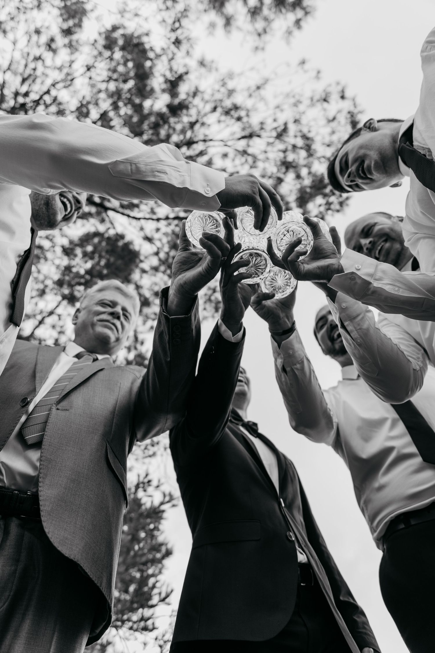 A low-angle black and white shot of people toasting with drinks in a celebratory circle.