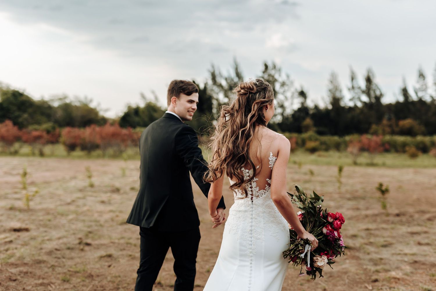Wedding couple poses in outdoor field with dramatic cloudy sky backdrop.