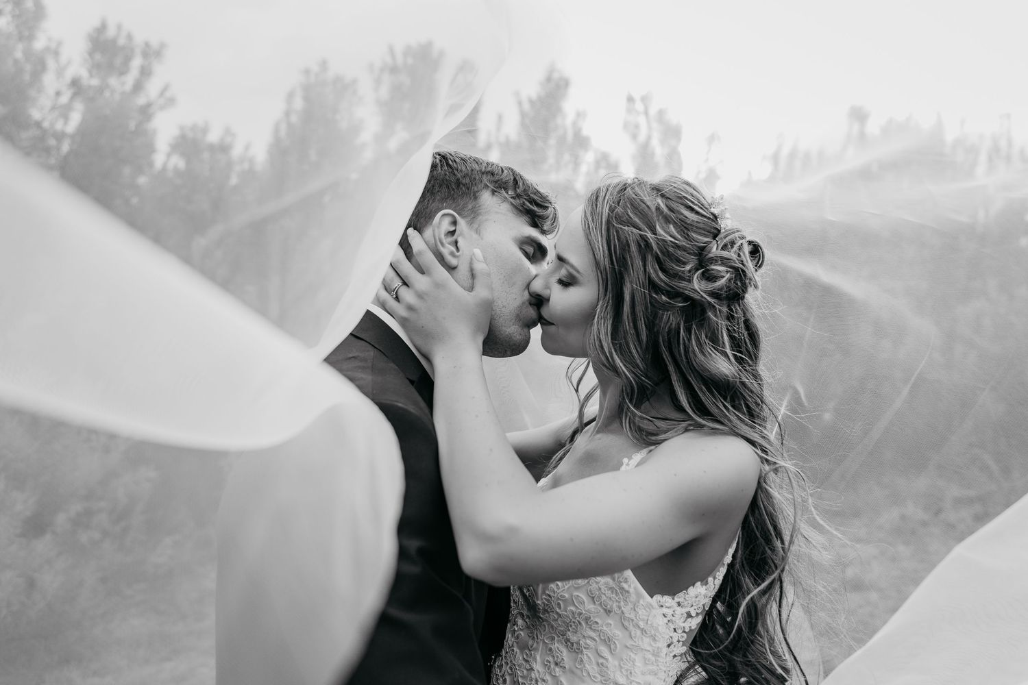 Black and white selfie of newlyweds sharing intimate kiss during wedding celebration.