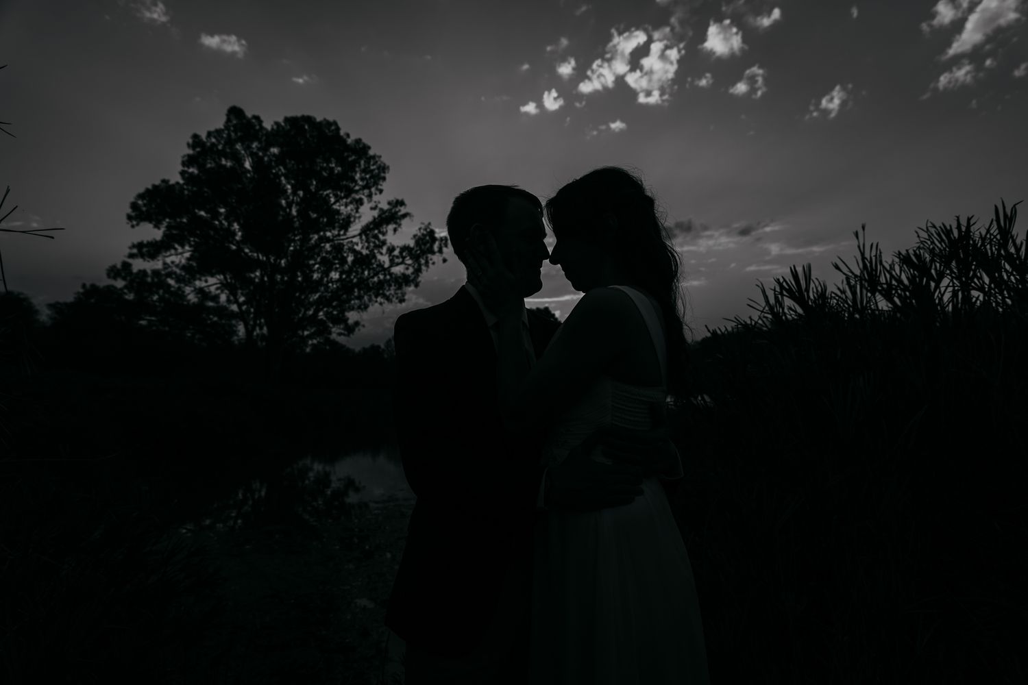 Silhouette of a bride and groom against a dramatic sky at sunset.