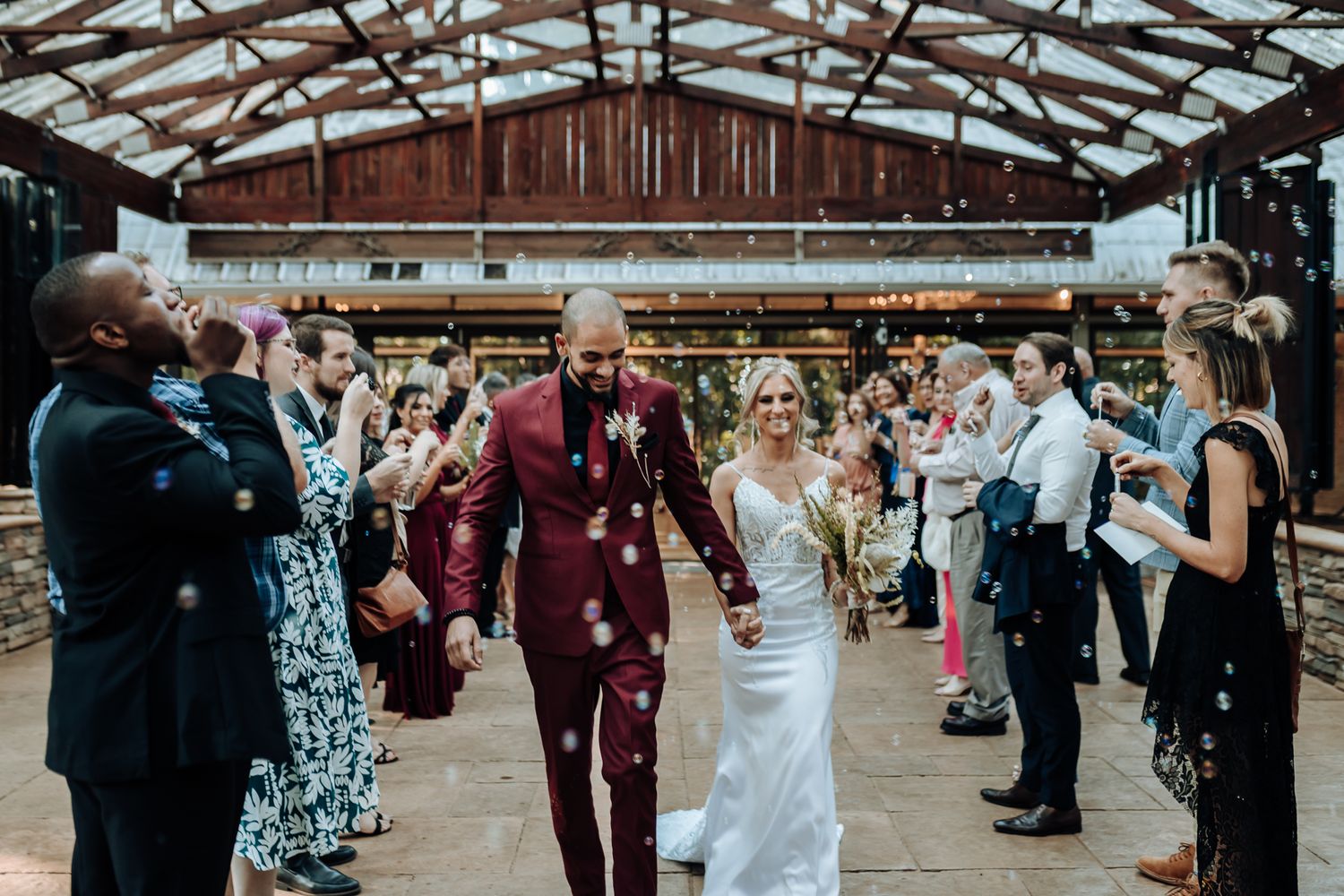 Wedding couple walks through guests in rustic indoor venue during celebration.