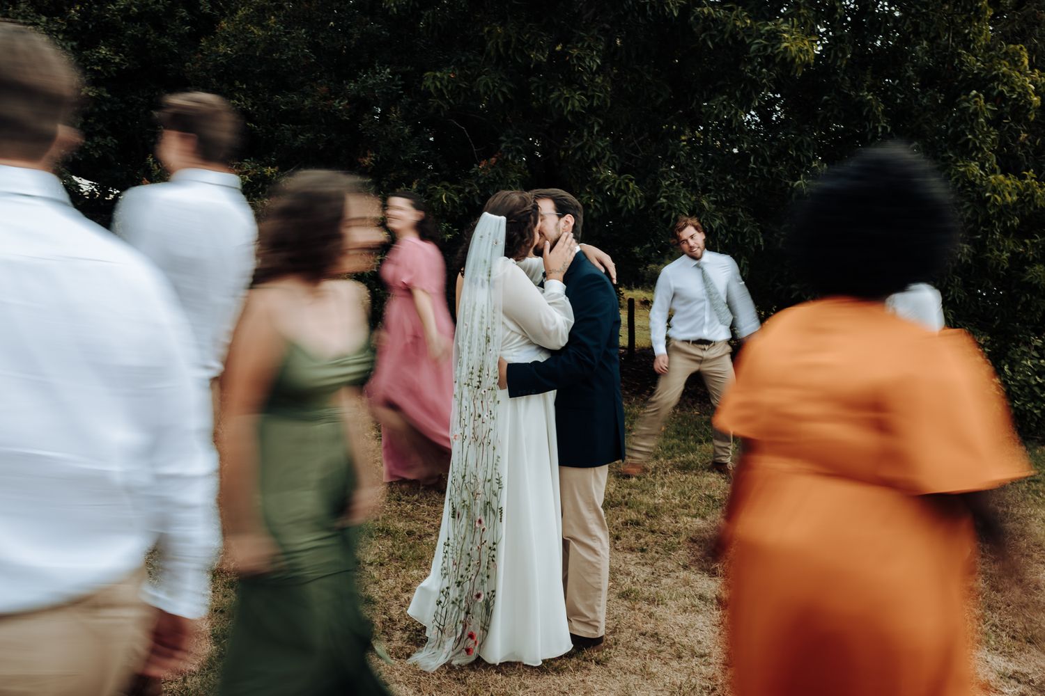 Couple embraces during wedding celebration as guests move around them in motion blur.