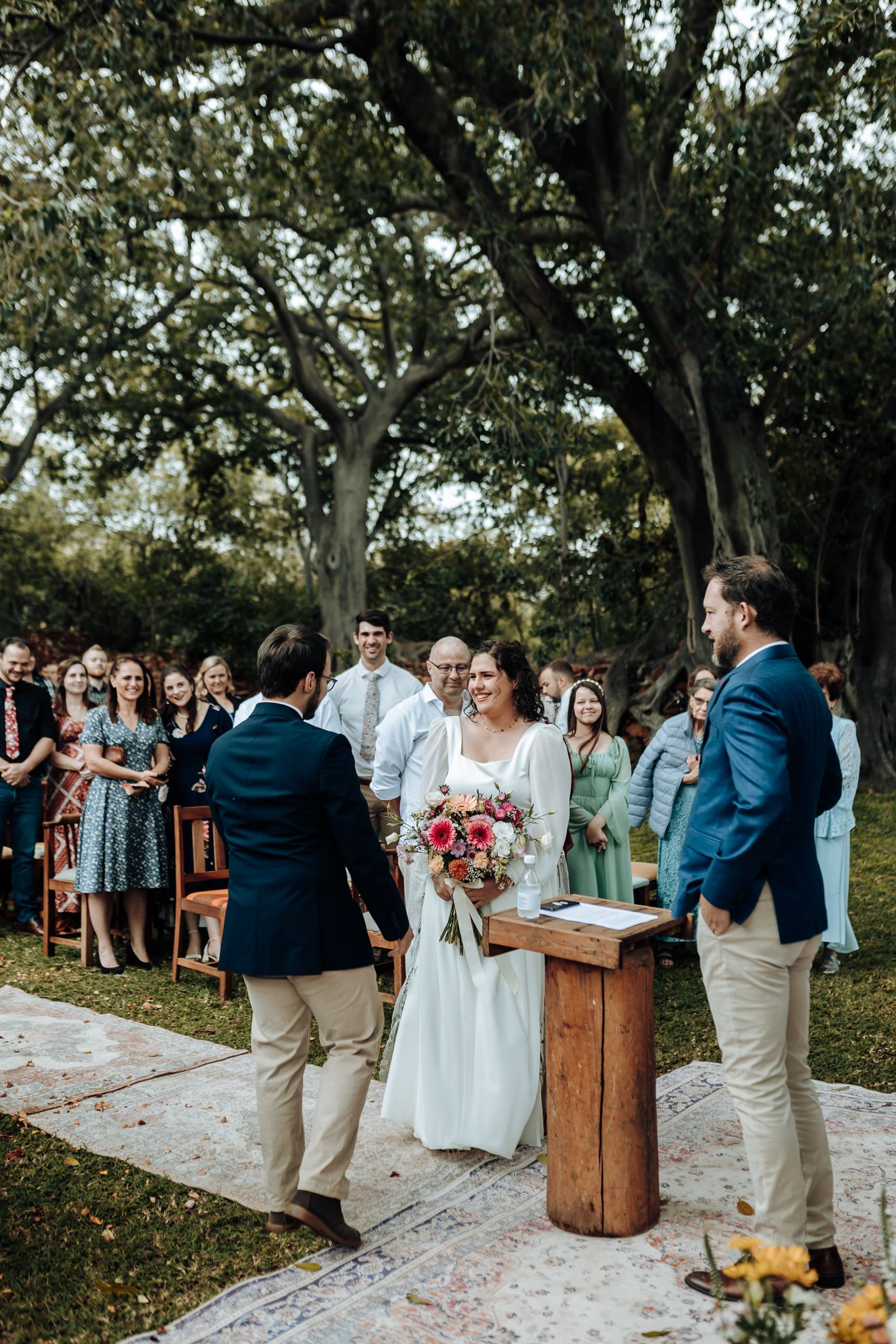 A wedding couple exchanges vows at a rustic outdoor ceremony with wooden furniture and natural decor.