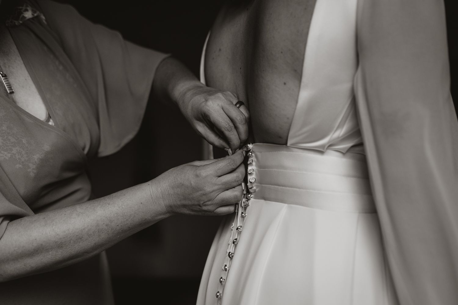 Close-up of hands fastening buttons on white wedding dress in black and white.