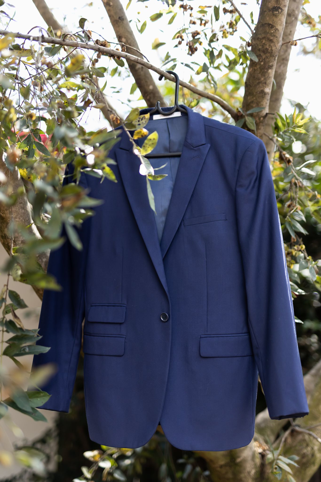 Navy blue suit jacket hanging on tree branch against green foliage.