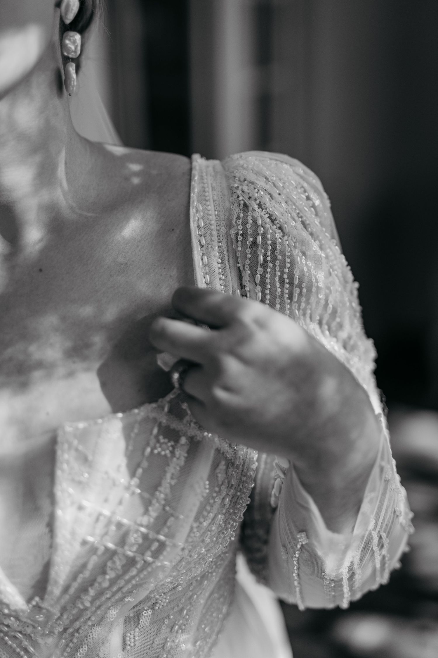 Close-up detail of intricate beaded lace sleeve on wedding dress with ring.
