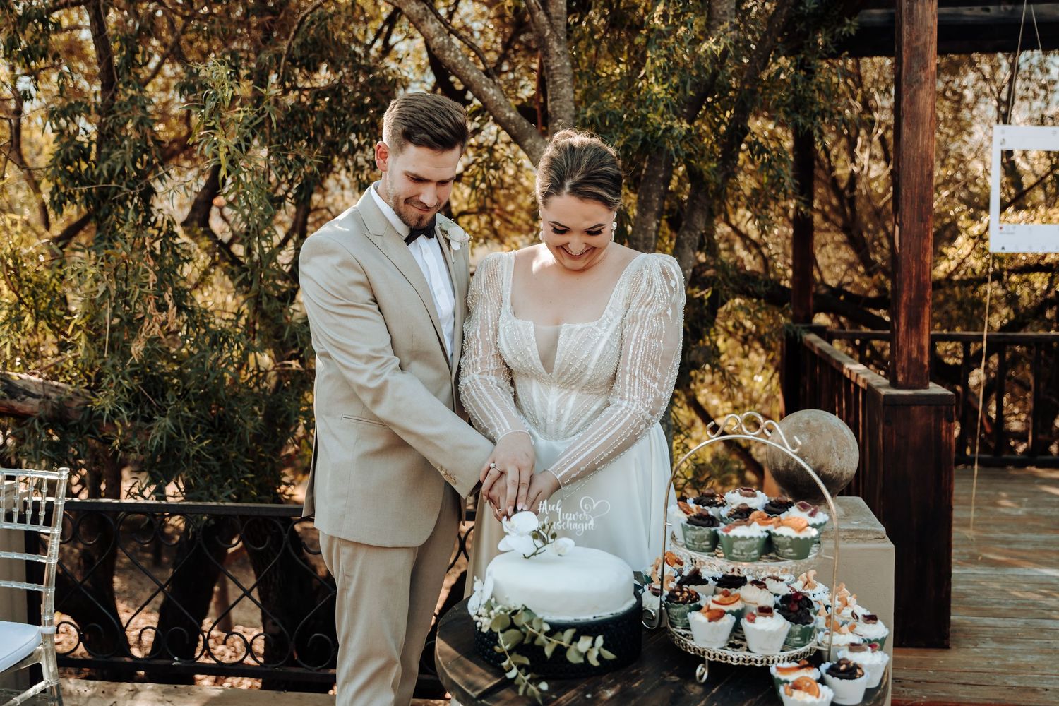 Couple cuts their elegant white wedding cake together at outdoor reception.