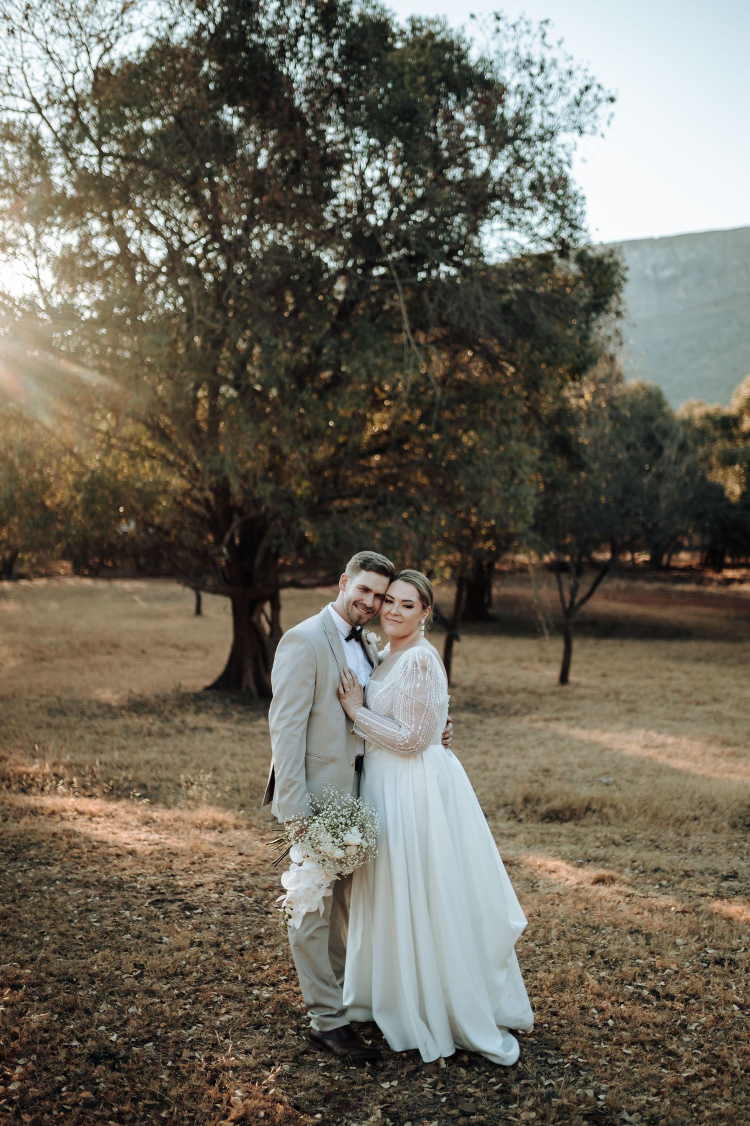 Beautiful outdoor wedding portrait with sunlit trees and mountains in background.