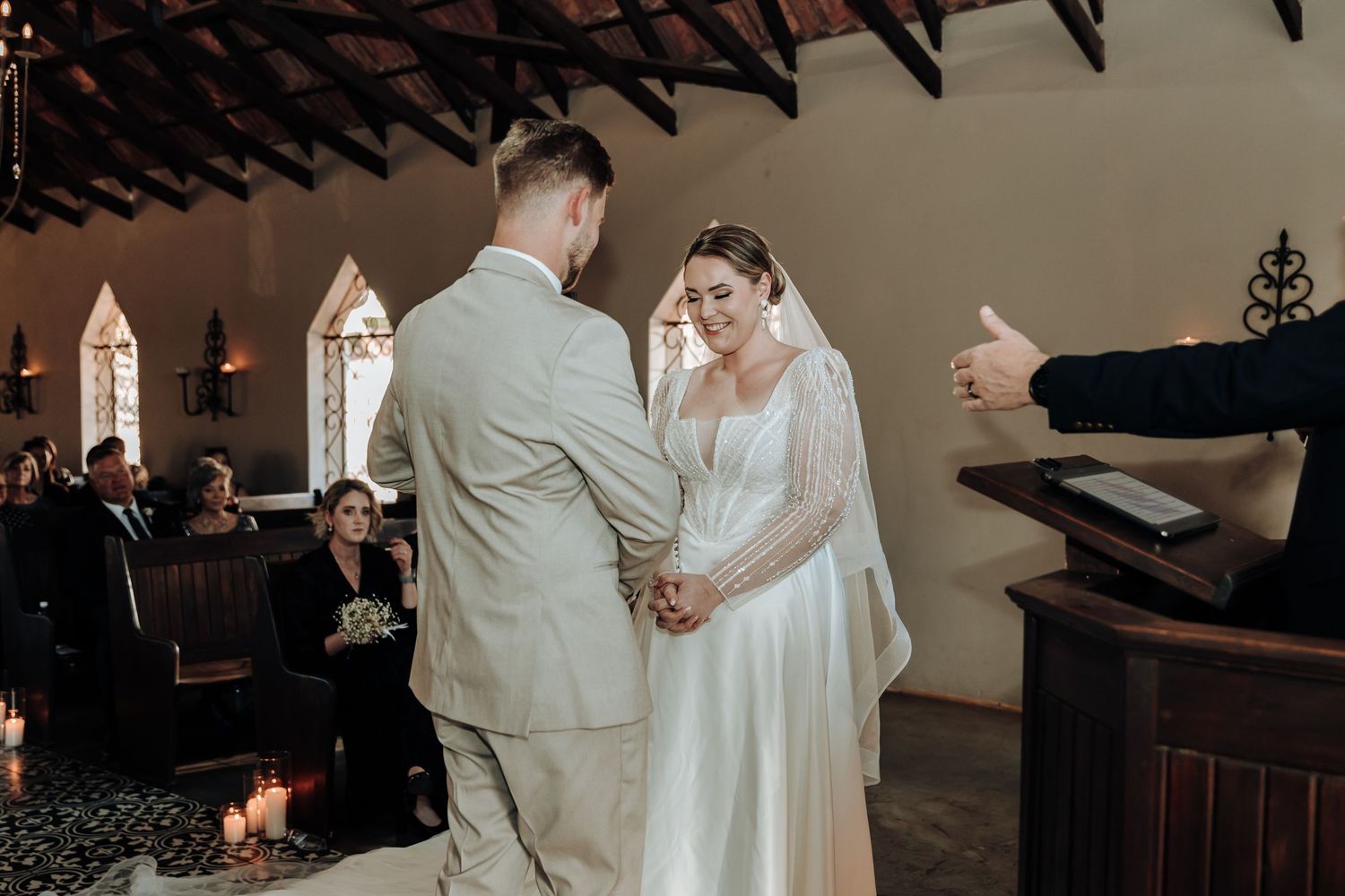 A couple exchanges vows during their wedding ceremony in a rustic chapel with wooden beams and gothic windows.