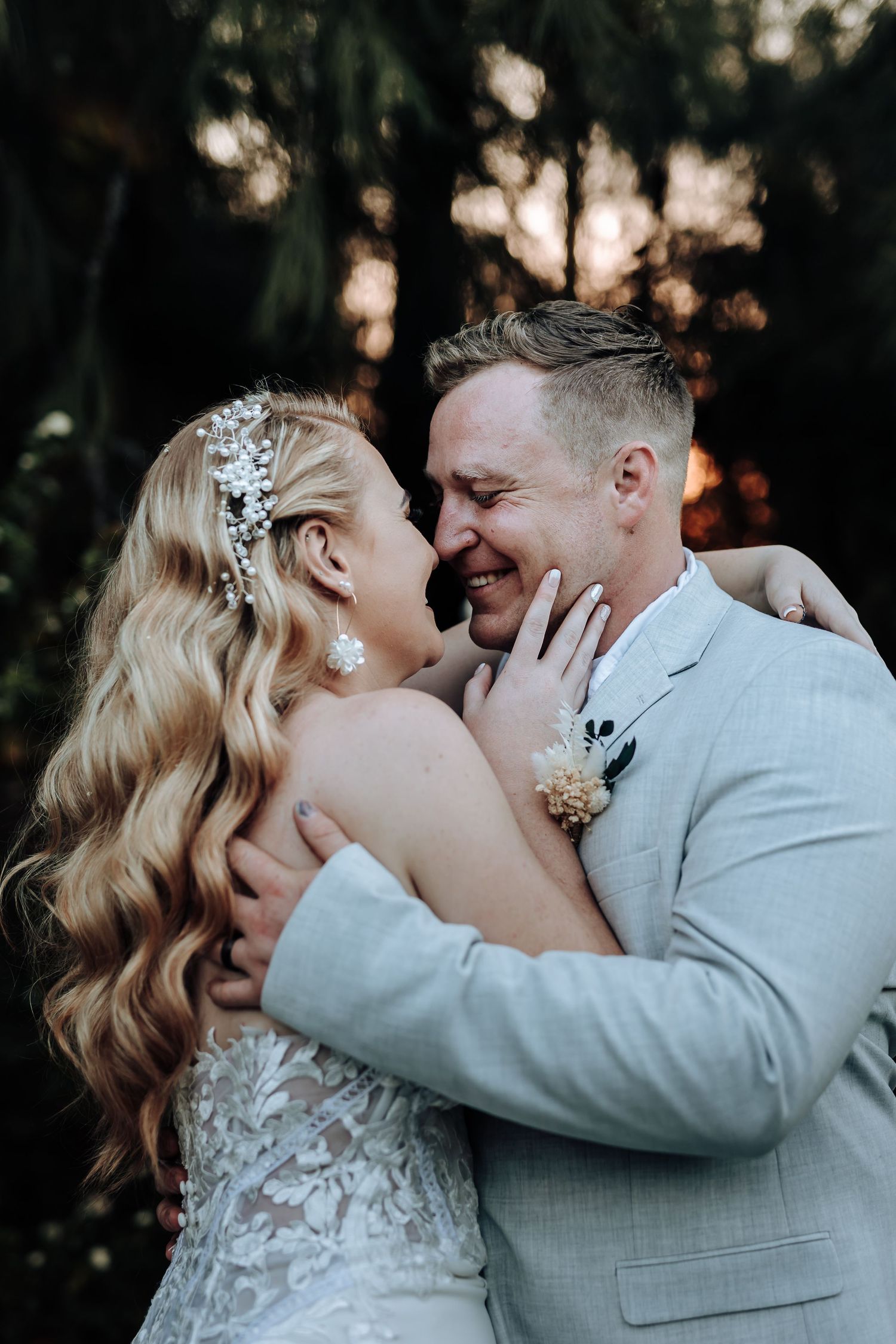 Intimate wedding moment captured in forest with couple embracing while wearing light gray suit and lace dress.