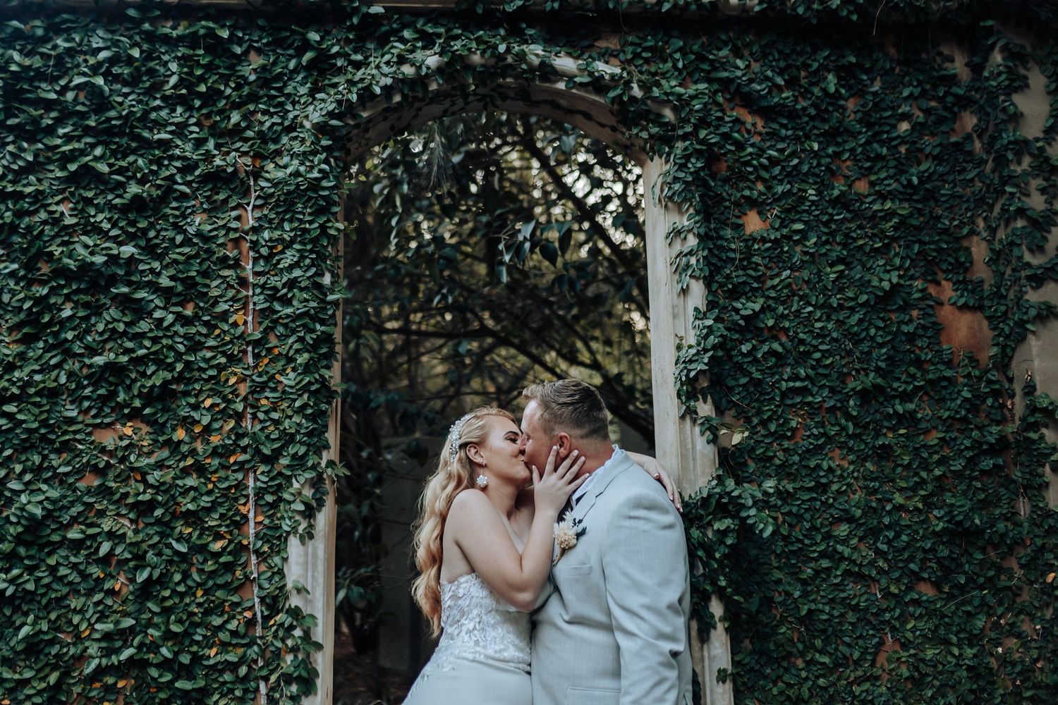 Wedding couple shares a tender moment in an ivy-covered archway.